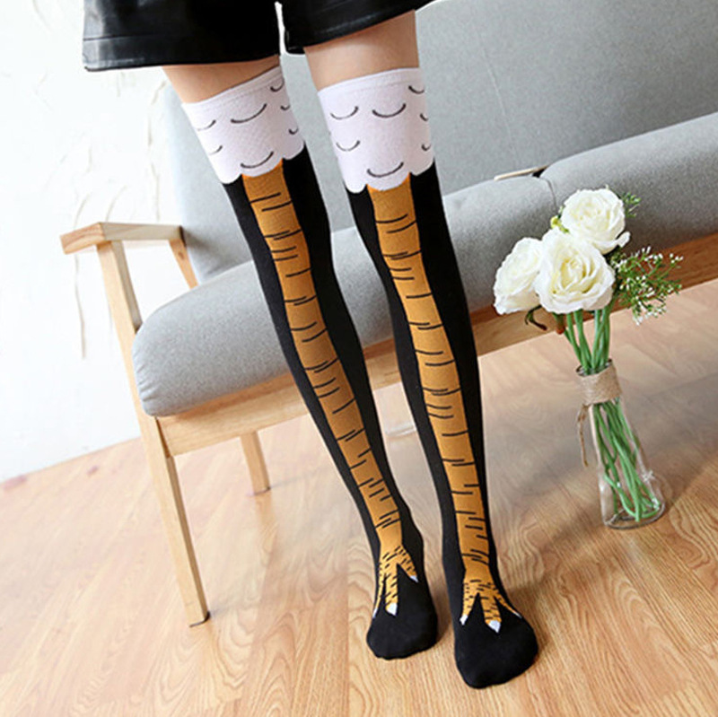 Model wearing novelty over-the-knee socks designed to look like bird legs, with yellow claw graphics on the feet, black shafts, and white tops featuring feather-like patterns.