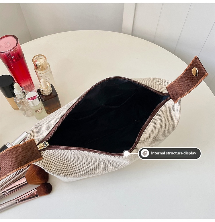 Open cream-white makeup bag showing the dark lining, wide zipped opening and brown handle tabs; cosmetics are not included