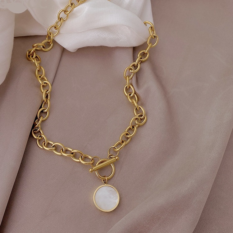 Gold chain bracelet with a round charm on a soft pink fabric background