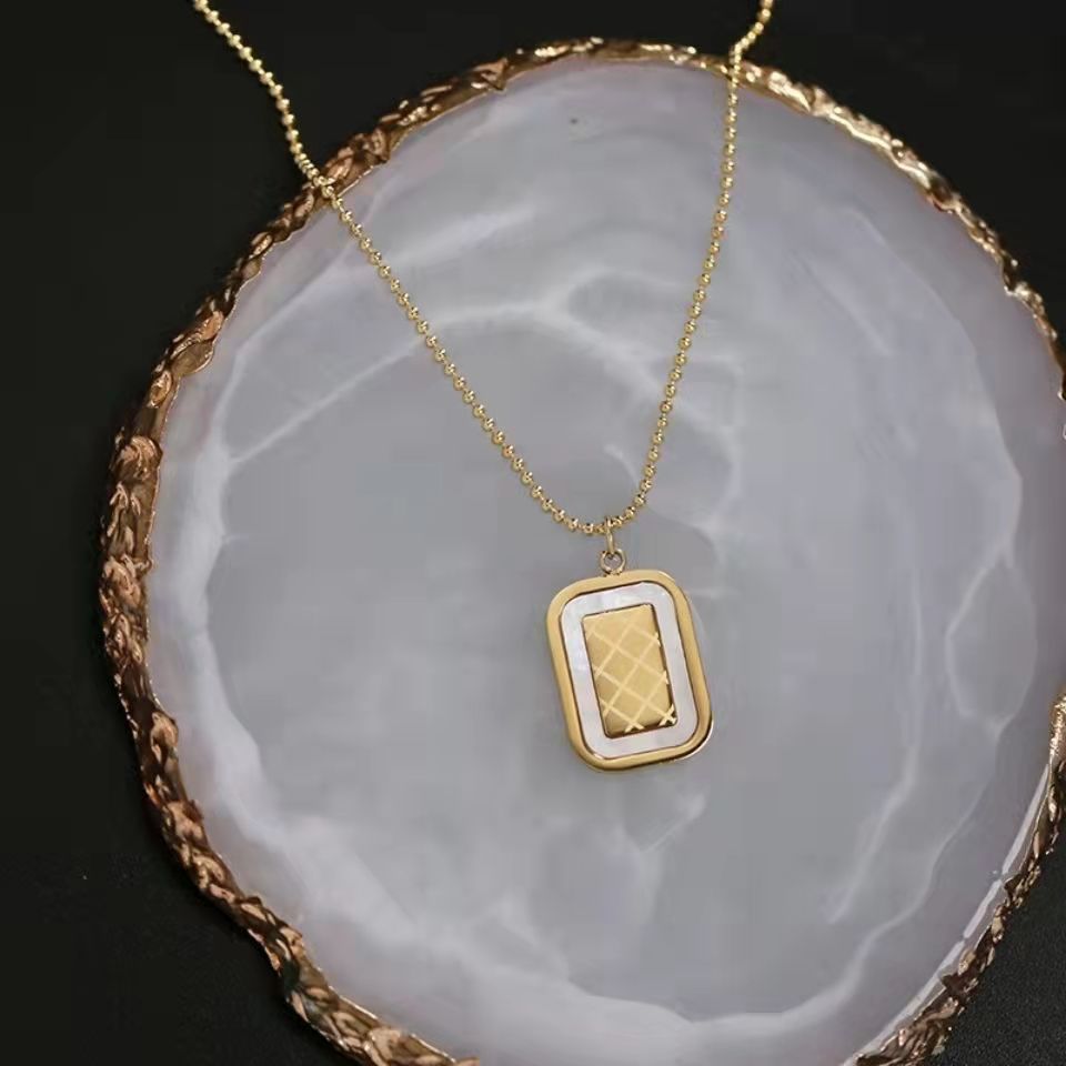 Gold necklace with a rectangular pendant on a decorative stone surface