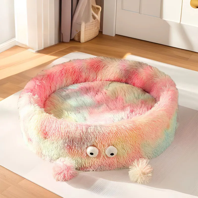 Fluffy pink and multicolored pet bed with googly eyes on a carpeted floor.