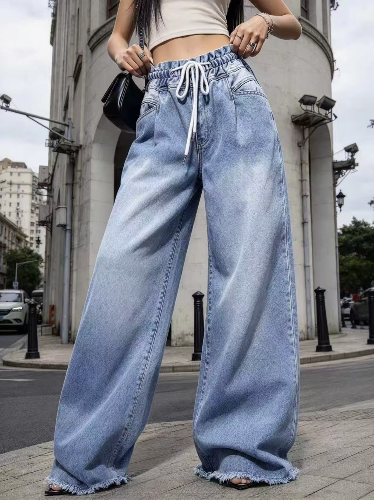 Closer front view of blue wide-leg jeans showing elastic waistband, white drawstring, pockets and frayed hems