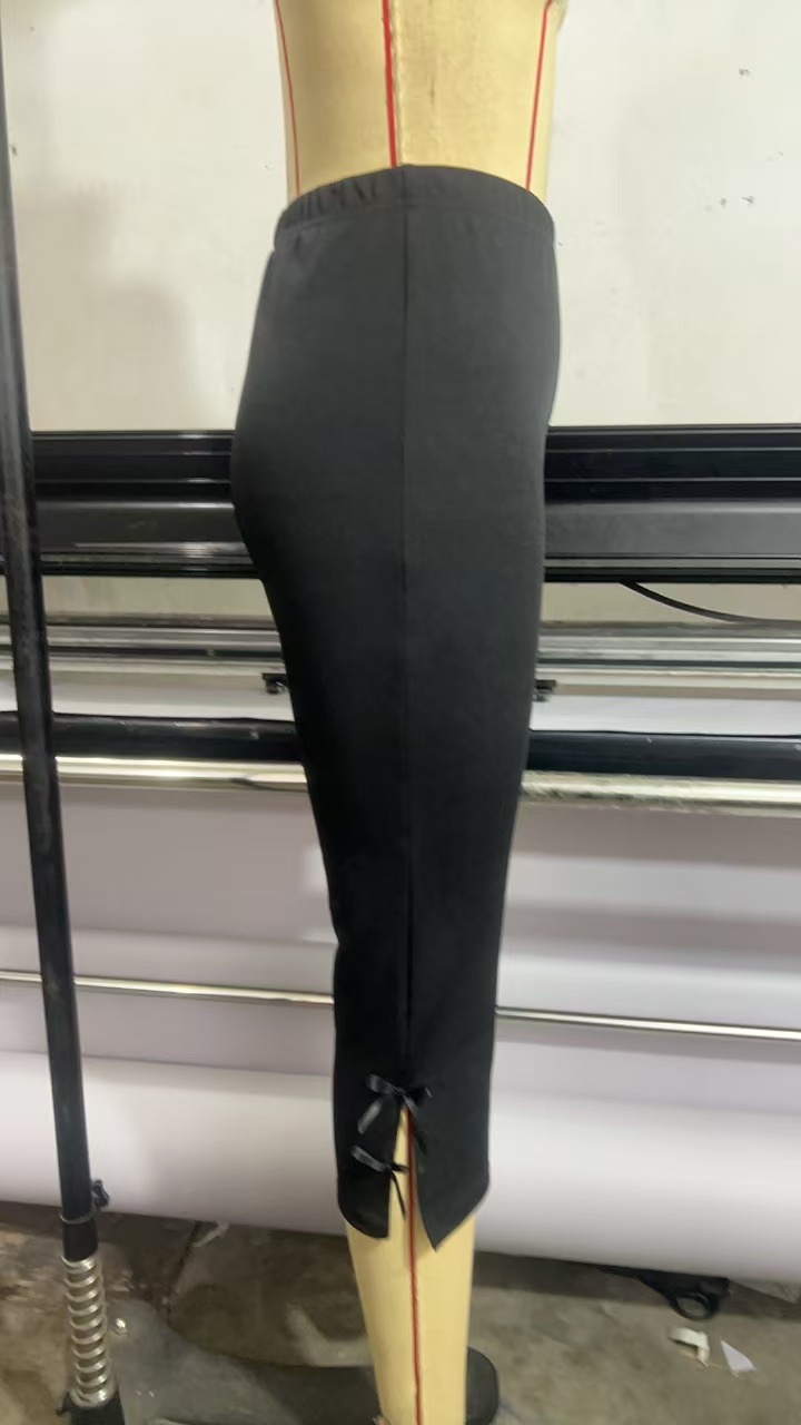 Actual black trousers on a dress form, showing the side-split cropped hem and small bow ties